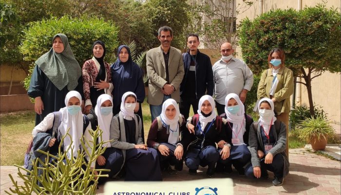 Eleven female and three male members of the Astronomical Clubs in Libya pose for a picture outdoors by trees and plants. The females are wearing head coverings.