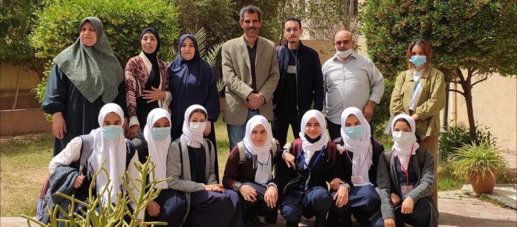 Eleven female and three male members of the Astronomical Clubs in Libya pose for a picture outdoors by trees and plants. The females are wearing head coverings.