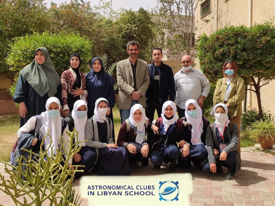 Eleven female and three male members of the Astronomical Clubs in Libya pose for a picture outdoors by trees and plants. The females are wearing head coverings.