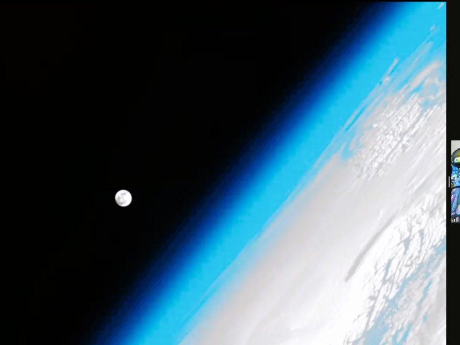 Astronomy for Equity. NASA Astronaut Nicole Stott gives an online live presentation in Libya, Africa. The screen shows a huge picture of Earth from space, off to the side, with Earth's atmosphere glowing in bright light blue along the border of the planet. The moon is a large dot against the blackness of space and next to Earth.