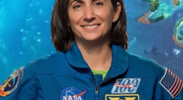 Astronomy for Equity. Former NASA Astronaut Nicole Stott is smiling and wearing a blue jumpsuit that has many patches on it including the American flag and NASA patches. She is standing in front of a blue-green background.