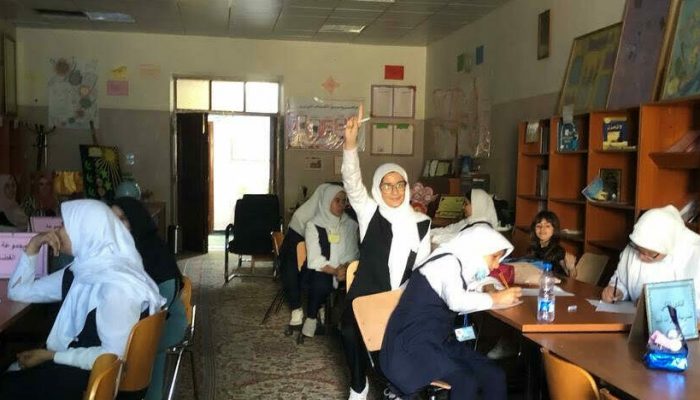 A female student in Libya smiles while raising her hand in a classroom of Libyan girls studying astronomy.