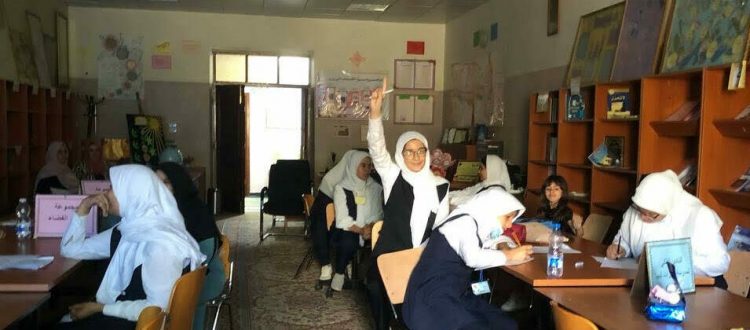 A female student in Libya smiles while raising her hand in a classroom of Libyan girls studying astronomy.