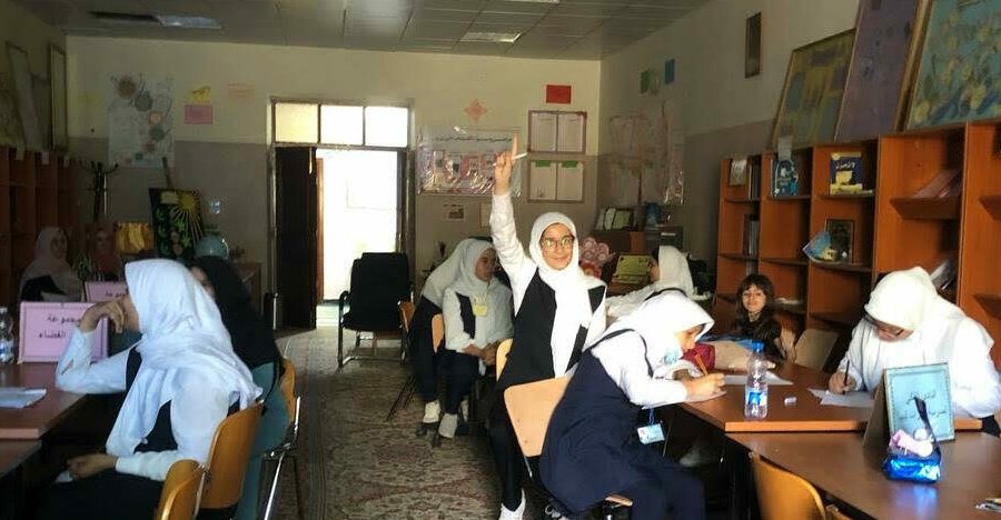 A female student in Libya smiles while raising her hand in a classroom of Libyan girls studying astronomy.