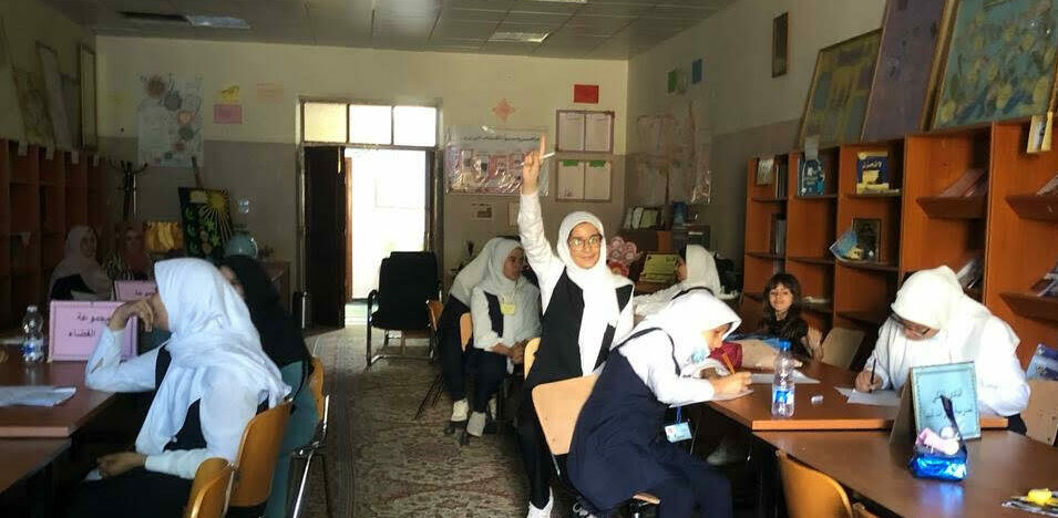 A female student in Libya smiles while raising her hand in a classroom of Libyan girls studying astronomy.